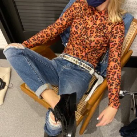 Woman in leopard print top and jeans sitting.