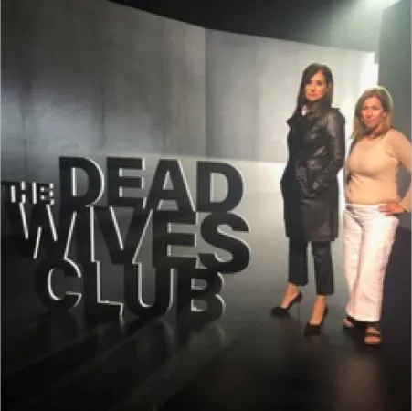 Two women standing by "The Dead Wives Club" sign.