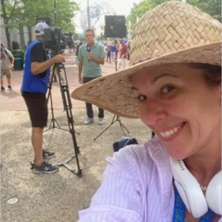 Woman in straw hat taking selfie with camera crew behind.