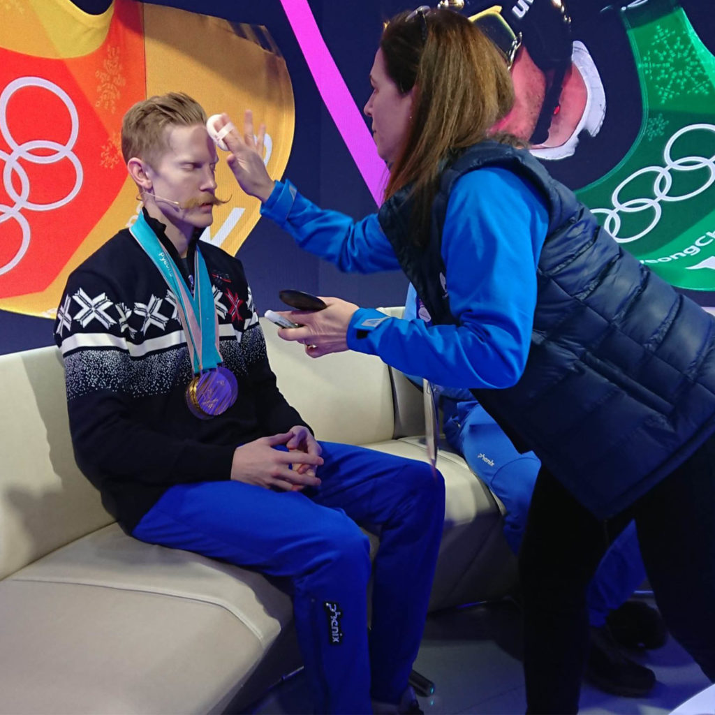 Athlete receiving makeup touch-up, Olympic medal visible.