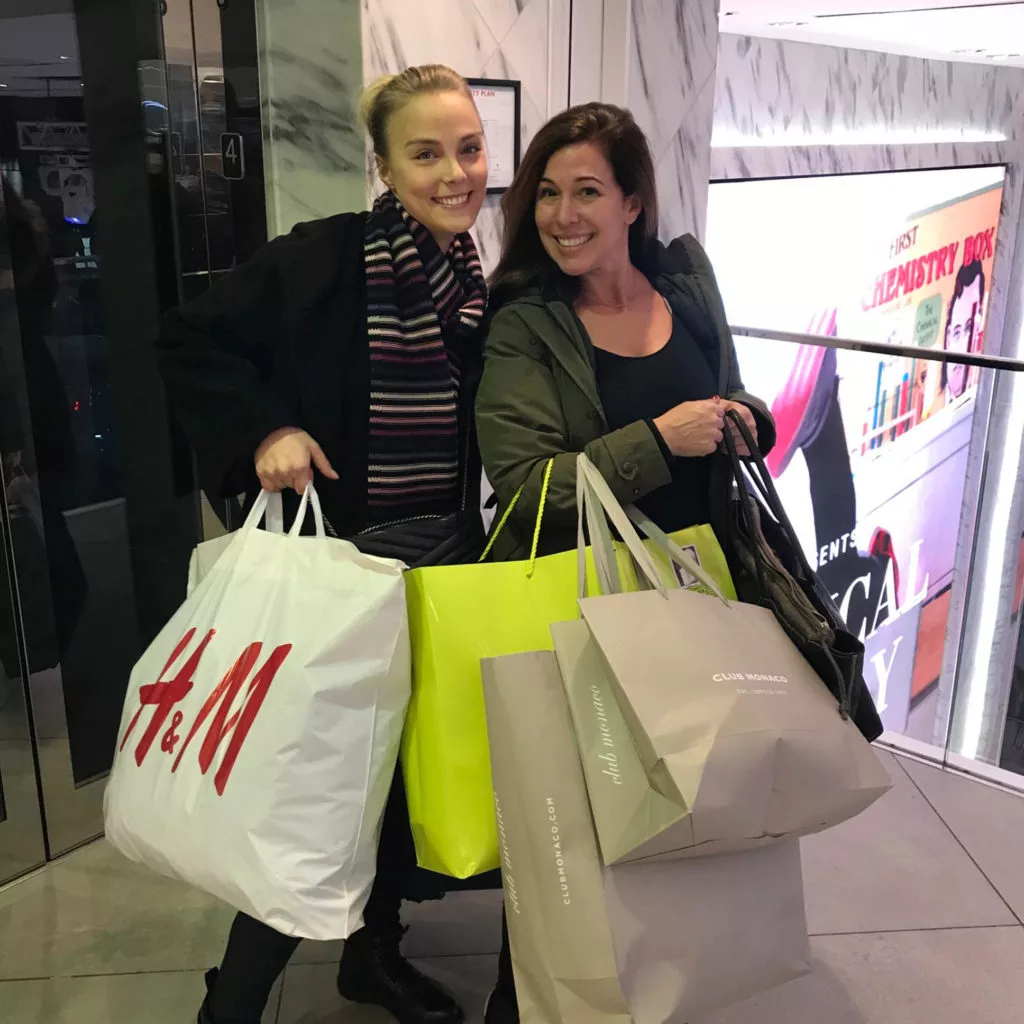 Two women smiling with shopping bags indoors.